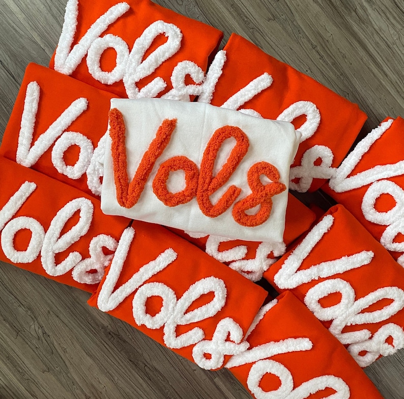 May include: A stack of orange fabric patches with white fluffy lettering that reads "VOLS" in various sizes and orientations.