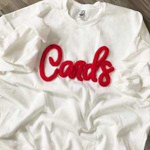 May include: White sweatshirt with a red fuzzy "Cards" logo.