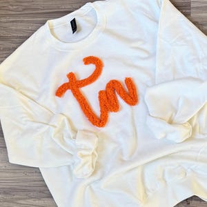 May include: White sweatshirt with a large orange fluffy "I'm" design.