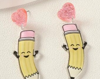 May include: A pair of novelty earrings featuring a yellow pencil design with a pink eraser and a smiling face. Each earring has a pink glitter heart at the top. The earrings are a fun and playful accessory.