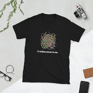Puede incluir: Camiseta negra con un gráfico colorido de cables de audio entrelazados. El texto blanco "It makes sense to me" está impreso debajo. Una camiseta unisex informal.