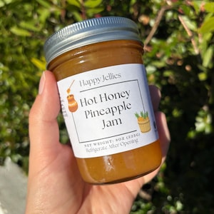 May include: A jar of "Happy Jellies" Hot Honey Pineapple Jam with a silver lid. The label includes illustrations of a honey pot and a pineapple. The net weight is 8oz (225g). The text "Refrigerate After Opening" is also on the label.