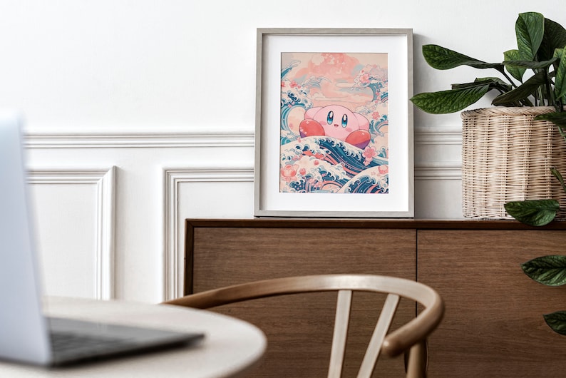 May include: A framed print of a pink cartoon character, Kirby, riding a large wave with a blue and white design. The wave is surrounded by pink flowers and a pink sky. The print is framed in a light gray frame and is sitting on a wooden shelf.