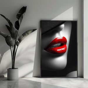 Op de afbeelding: Zwart-wit ingelijste kunstafdruk met een close-up van een vrouwengezicht met felrode lippen. Het kunstwerk is een opvallend contrast van zwart, wit en rood, met de nadruk op de lippen en de schaduw van een hoed.