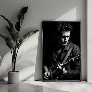 Op de afbeelding: Een zwart-wit ingelijste muurkunstprint met een persoon die een elektrische gitaar bespeelt. Het onderwerp is vanaf de borst afgebeeld, draagt een overhemd met kraag en een gitaarband over de schouder, vastgelegd in een sfeervolle belichting.