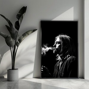 Puede incluir: Fotografía en blanco y negro de una persona fumando un cigarrillo. La persona mira hacia un lado y tiene el pelo largo. La foto está enmarcada en un marco negro.
