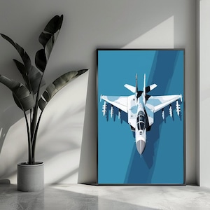 Può includere: Una stampa artistica incorniciata con un'illustrazione stilizzata di un jet da combattimento bianco e blu su sfondo blu. L'opera d'arte è esposta su una parete accanto a una pianta in vaso con grandi foglie verde scuro.