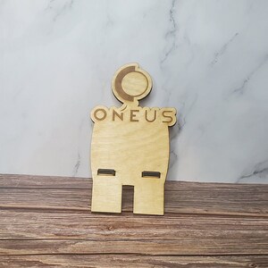 May include: A wooden stand with two slots for holding items. The stand is shaped like a person with a circle on its head and the word "ONEUS" written on its chest.