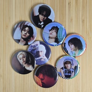 May include: Eight round button pins featuring different portraits of young men. The buttons are colorful and feature various backgrounds, including a blue sky, a cactus, and a mountain range.