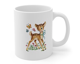 May include: White ceramic mug with a colorful illustration of a fawn with a blue bow, surrounded by butterflies and flowers.