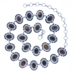May include: Silver-toned metal belt with oval, brown-toned stones set in decorative frames. The belt features a chain extension and a clasp closure. The design is intricate and detailed, suitable for adding a touch of flair to any outfit.
