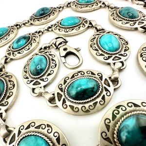 May include: Silver-coloured belt with oval turquoise-coloured stones set in decorative frames. The belt has a clasp closure and is designed with a series of connected oval links. The stones have a marbled appearance.
