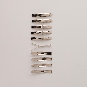May include: A set of 12 silver hair clips, arranged in a vertical line on a white background.
