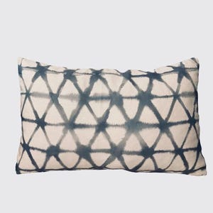 May include: Rectangular decorative pillow with a cream-colored background and a repeating geometric pattern in shades of blue. The pattern consists of interconnected triangles, creating a textured appearance. The pillow is designed for home decor.