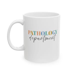May include: White ceramic mug with the words "PATHOLOGY department" in colorful text. The word "PATHOLOGY" is in a multi-colored font, and "department" is in a black script font. The mug has a curved handle.