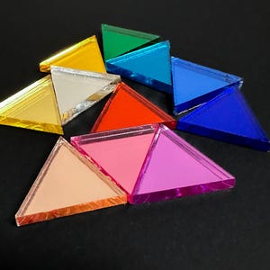 Könnte beinhalten: Eine Ansammlung farbenfroher, dreieckiger Acrylformen in verschiedenen Farben, darunter Gelb, Grün, Blau, Rot, Rosa und Orange. Die Formen sind auf einer dunklen Oberfläche angeordnet und erzeugen eine lebendige und auffällige Darstellung. Diese geometrischen Formen eignen sich ideal zum Basteln oder Dekorieren.