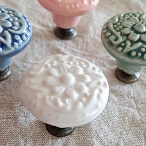 May include: Four ceramic drawer knobs with intricate floral designs. The knobs are in shades of pink, blue, green, and white.