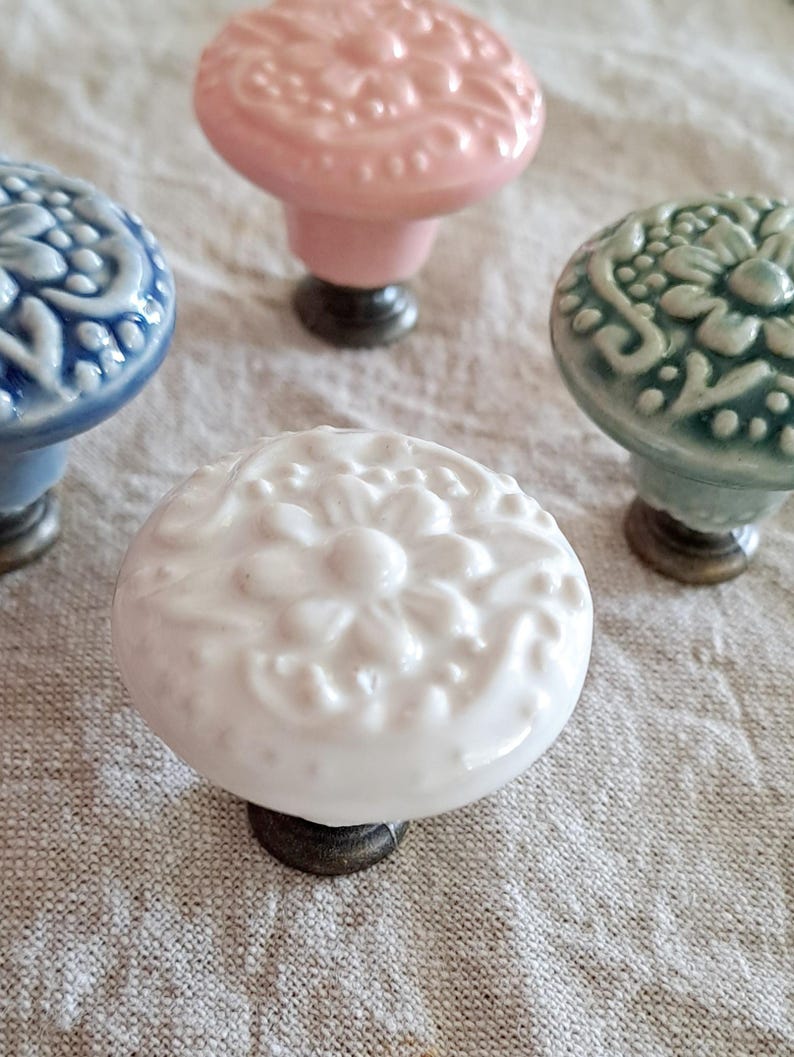 May include: Four ceramic drawer knobs with intricate floral designs. The knobs are in shades of pink, blue, green, and white.