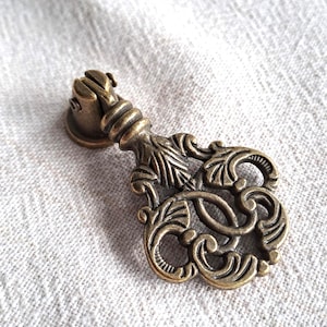 May include: An antique brass drawer pull with an elaborate floral design. The pull has a decorative handle and a round base, ideal for adding a vintage touch to furniture. The brass finish gives it a classic, aged appearance.