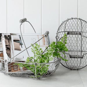 May include: A wire mesh basket with a handle, filled with magazines and greenery. A second, round wire mesh container is behind the basket. The items are on a white surface with a white background.