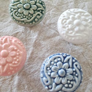 May include: Four ceramic knobs with floral designs. The knobs are in shades of green, white, pink, and blue.