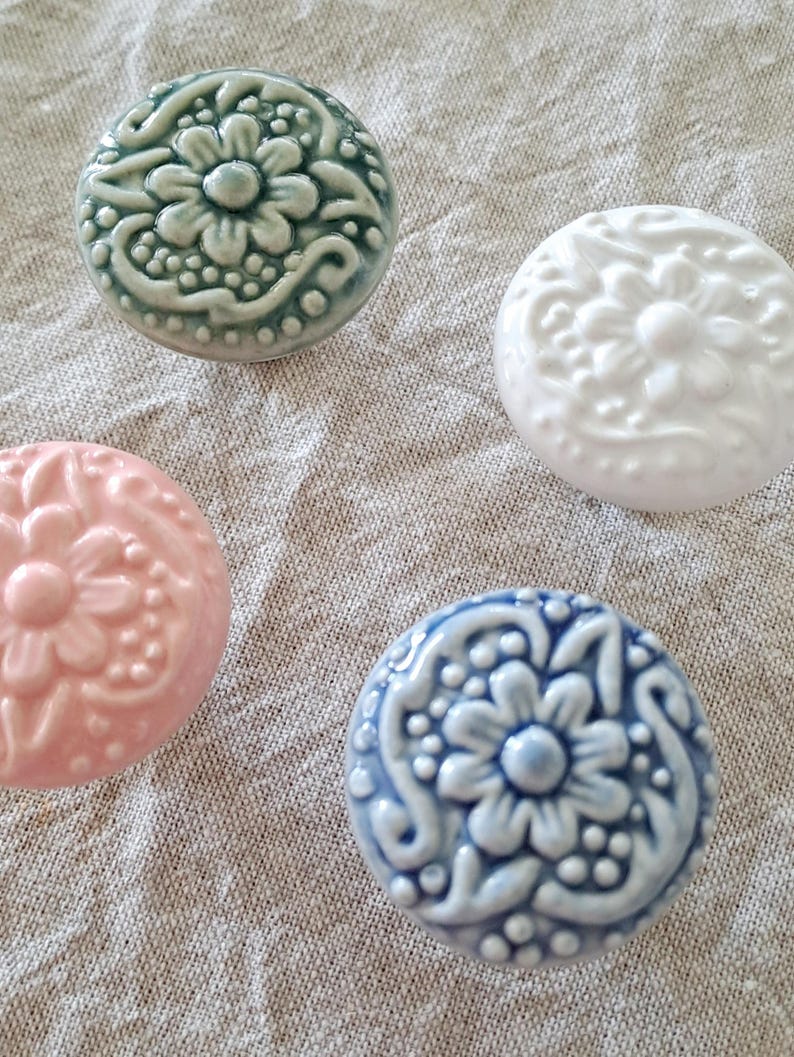 May include: Four ceramic knobs with floral designs. The knobs are in shades of green, white, pink, and blue.