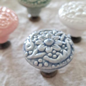 May include: Four ceramic cabinet knobs with floral designs. The knobs are in shades of light blue, white, pink, and green.