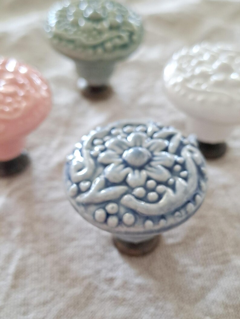 May include: Four ceramic cabinet knobs with floral designs. The knobs are in shades of light blue, white, pink, and green.