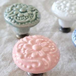 May include: Four ceramic drawer knobs with floral designs. The knobs are in shades of white, light blue, pink, and blue. Each knob has a raised floral design.