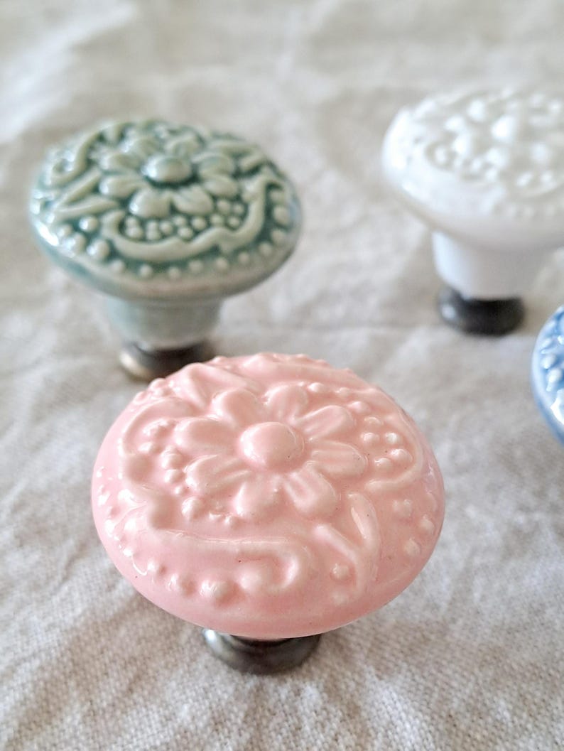 May include: Four ceramic drawer knobs with floral designs. The knobs are in shades of white, light blue, pink, and blue. Each knob has a raised floral design.