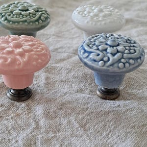 May include: Four ceramic cabinet knobs with a floral design. The knobs are in shades of green, white, pink, and blue.