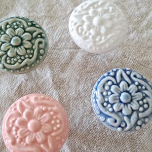 May include: Four ceramic knobs with a floral design. The knobs are in shades of white, blue, green, and pink.