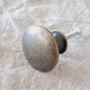May include: A bronze oval cabinet knob with a matching base and a silver screw. The knob has a slightly aged appearance, suggesting a vintage or antique style. The hardware is designed for furniture or cabinetry.