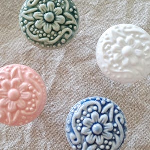 May include: Four ceramic knobs with floral designs. The knobs are in shades of blue, green, pink, and white.