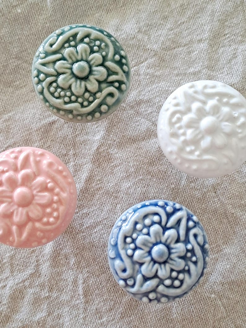 May include: Four ceramic knobs with floral designs. The knobs are in shades of blue, green, pink, and white.