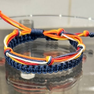 May include: A multi-colored friendship bracelet with blue, white, orange, and yellow threads woven together in a knot pattern.