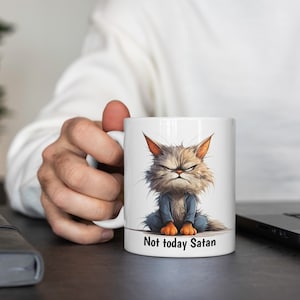 May include: White ceramic mug featuring a cartoon illustration of an angry cat wearing a blue shirt. The text "Not today Satan" is printed on the bottom of the mug.