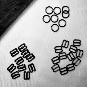 May include: A close-up of black metal bra strap adjusters and rings. The adjusters are in the shape of a figure eight and the rings are round.