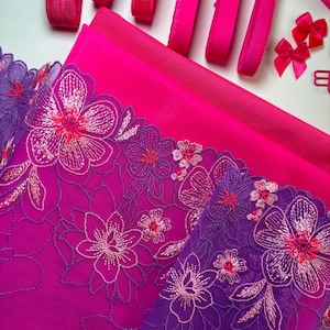 Op de afbeelding: Roze en paarse bloemenkant met roze satijnen lint en roze elastische trim. Deze stof is perfect voor knutsel- en naaiprojecten.
