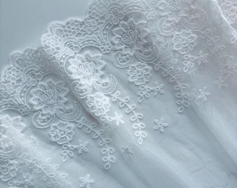 Puede incluir: Primer plano de tela de encaje blanco con intrincados patrones florales y de hojas. El encaje presenta un borde festoneado y está hecho de un material delicado y transparente. El diseño incluye bordados detallados.