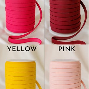May include: Four spools of elastic ribbon in various colors: hot pink, wine, yellow, and pink. Each spool is labeled with its color name in capital letters. The ribbon is neatly rolled and displayed against a white background.