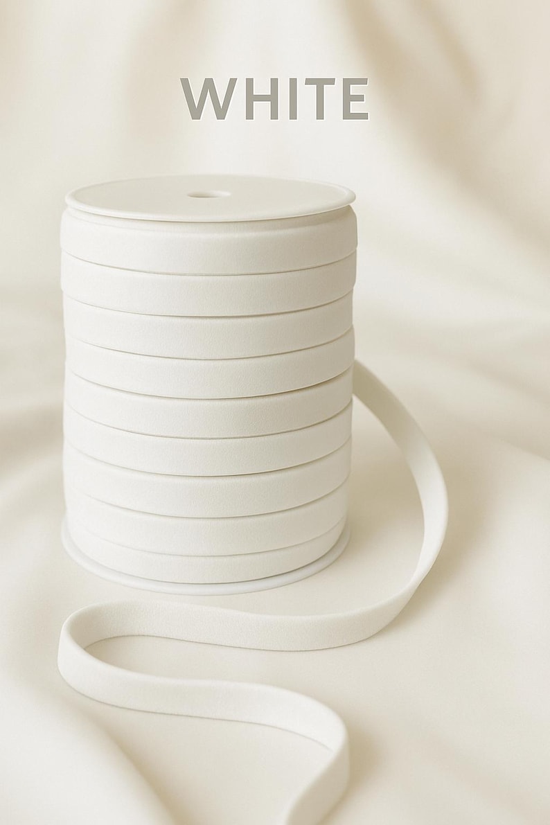 May include: A spool of white elastic ribbon, with the word "WHITE" in gray text at the top. The ribbon is neatly coiled, with a length of the ribbon extending outwards. The background is a soft, white fabric.