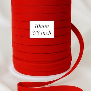 May include: A spool of bright red bias tape, 10mm (3/8 inch) wide, is displayed against a white background. The text "10mm 3/8 inch" is printed on a white square. A selection of color swatches is shown below.