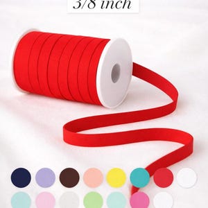 Könnte beinhalten: Eine Rolle rotes elastisches Band, 10 mm breit, abgewickelt, um das Material zu zeigen. Das Bild enthält eine Farbpalette verschiedener runder Farben, darunter Marine, Lavendel, Braun, Pfirsich, Gelb, Türkis, Rosa und Weiß.