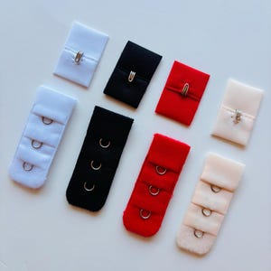 May include: Assortment of bra extenders in various colors, including white, black, red, and beige. The extenders feature hook-and-eye closures and are designed to add extra length to bra straps for a more comfortable fit.