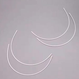 May include: Two pairs of white metal bra underwires, each pair is curved and shaped like a crescent moon.