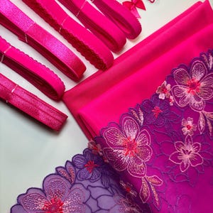Op de afbeelding: Een set met roze elastische trim, roze stof en paars-roze bloemenkant. De stof is effen roze en de kant heeft een verloop van paars naar roze.