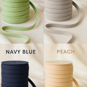 May include: Four spools of elastic ribbon in Paradise Green, Grey, Navy Blue, and Peach. Each spool is tightly wound, with a length of ribbon extending from the top. The colors are labeled with text above each spool.