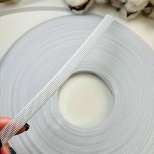 May include: A roll of white elastic with a textured surface. The elastic is approximately 1/2 inch wide.