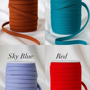 May include: Four spools of elastic ribbon in various colors: brown, teal, sky blue, and red. Each spool is labeled with its respective color name in a white font. The ribbon is neatly wound on white spools.